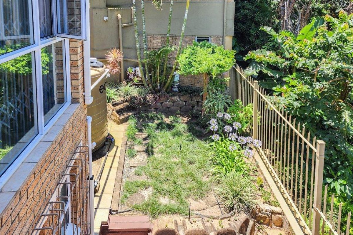 A view of the rear garden area featuring a water storage tank, retaining wall, and metal perimeter fencing alongside the brick building exterior.