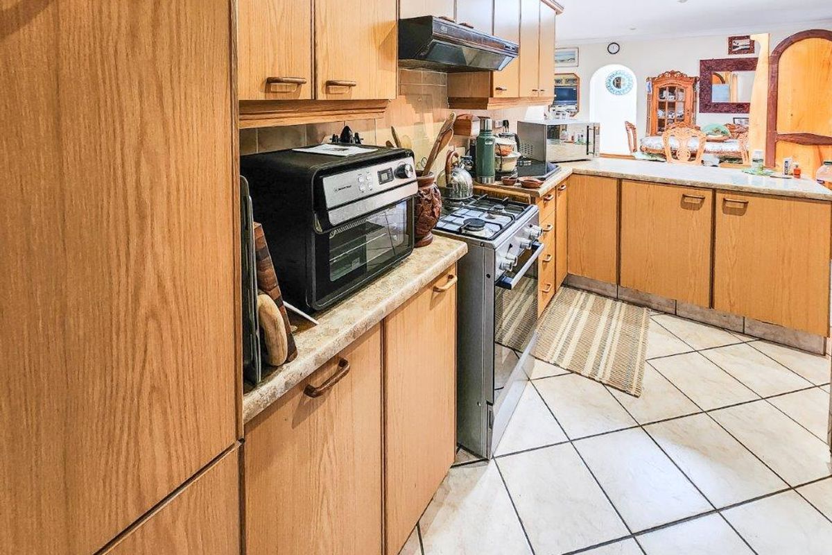 A functional kitchen featuring wood-look laminate cabinetry, gas stove with extractor fan, and tiled flooring, offering a traditional layout with ample storage space.