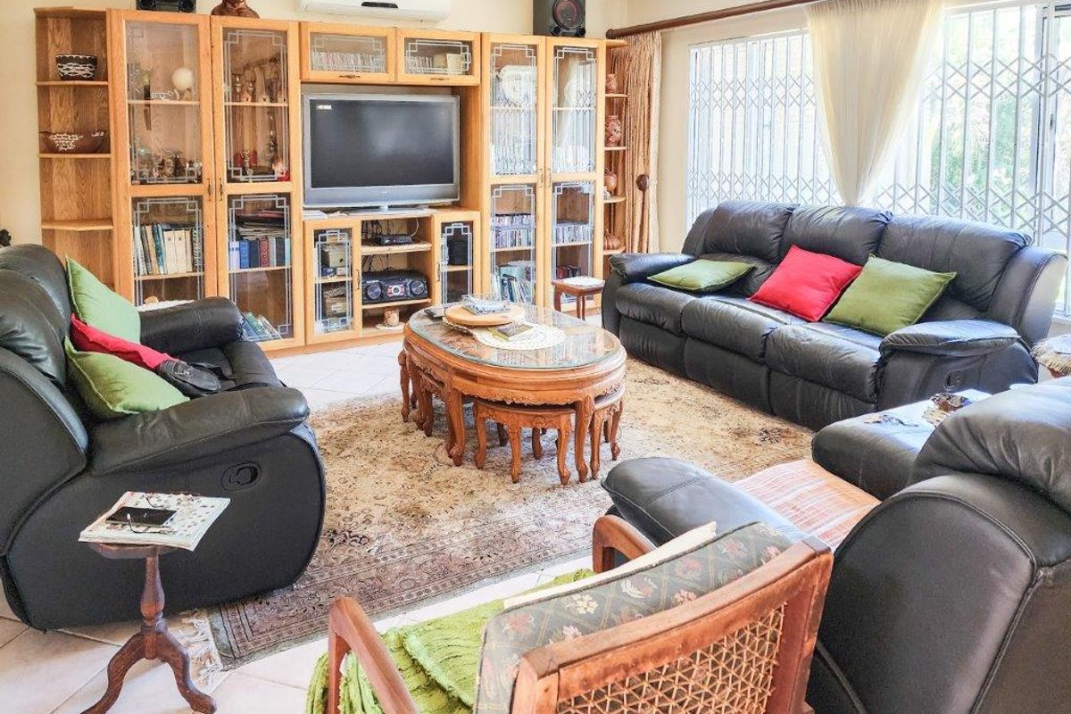 A spacious living room featuring built-in wooden cabinetry, tiled flooring, and a wall-mounted air conditioning unit, with large windows secured by metal gates.