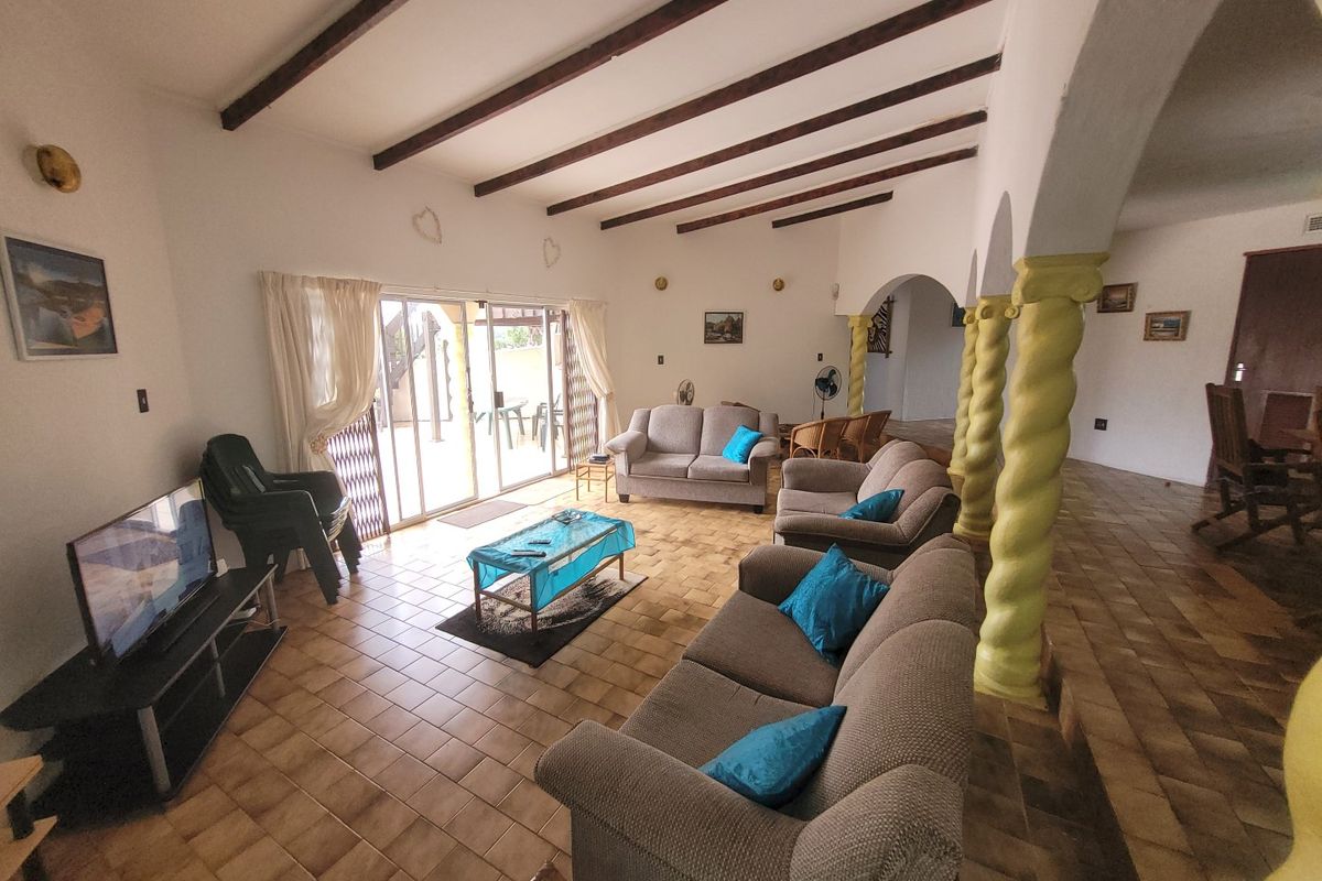 Spacious living room featuring exposed timber ceiling beams, ceramic tiled flooring, and decorative spiral columns leading to an outdoor patio area.