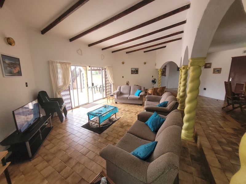 Spacious living room featuring exposed timber ceiling beams, ceramic tiled flooring, and decorative spiral columns leading to an outdoor patio area.