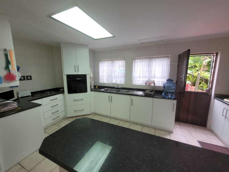 A functional kitchen featuring white cabinetry, dark granite countertops, a built-in oven, and a double sink with direct access to the exterior.