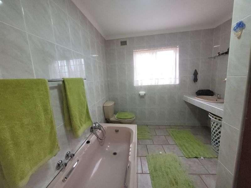 A functional bathroom featuring a built-in bathtub, wall-mounted toilet, and vanity basin with full-height wall tiling.