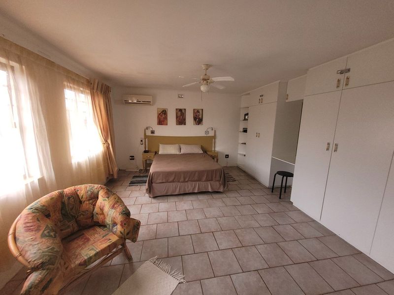 Spacious bedroom featuring built-in cupboards, tiled flooring, a ceiling fan, and an air conditioning unit for climate control.