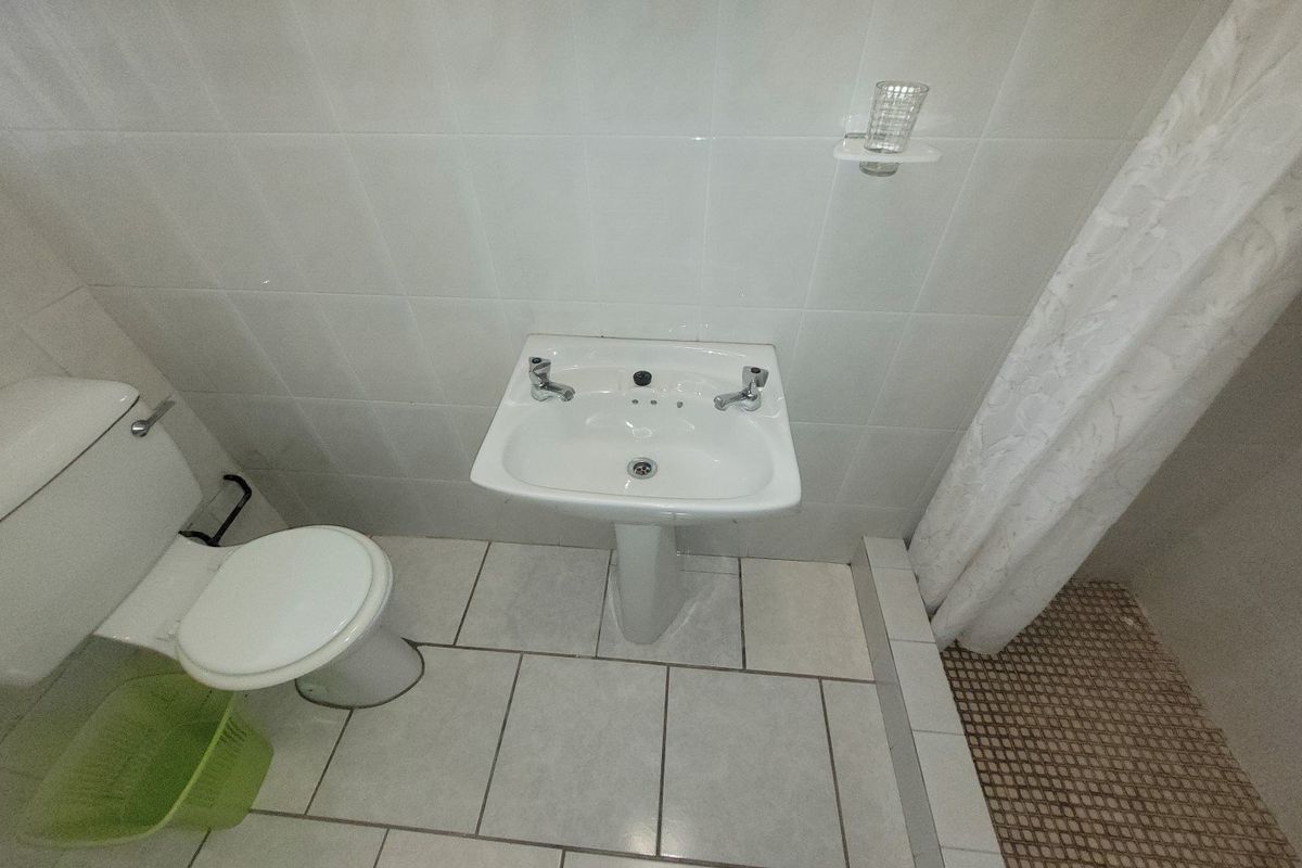 A functional bathroom featuring a pedestal basin, toilet, and shower area with tiled finishes.