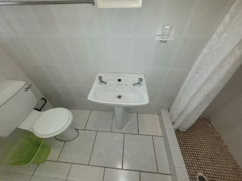 A functional bathroom featuring a pedestal basin, toilet, and shower area with tiled finishes.