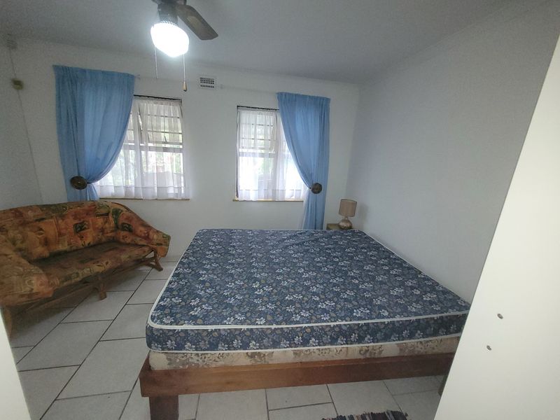 A bedroom featuring tiled flooring and a ceiling fan, with two windows providing natural light.