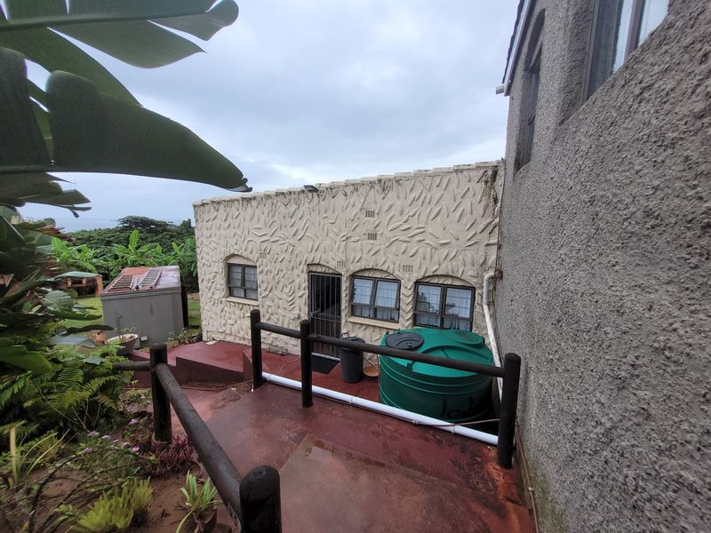 Rear exterior view of the townhouse featuring a textured facade, paved patio area with timber railings, and a large water storage tank.