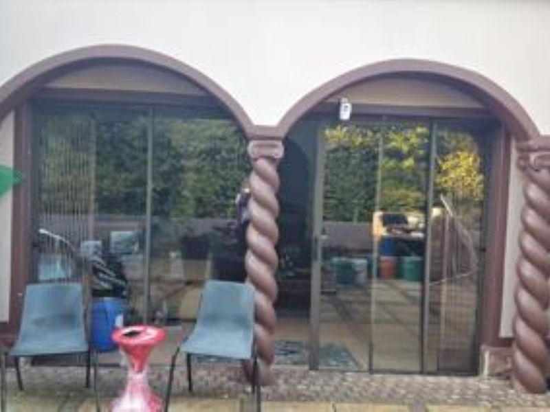 A covered patio area featuring distinctive decorative spiral columns, arched architectural detailing, and sliding glass doors providing access to the interior living space.