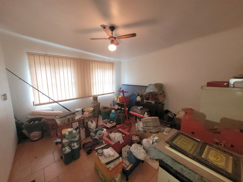 A bedroom featuring tiled flooring, a ceiling fan, and vertical blinds, currently used for storage.