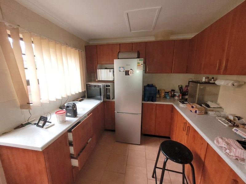 A functional kitchen featuring wood-tone cabinetry, laminate countertops, and tiled flooring, offering a practical layout with ample storage space.