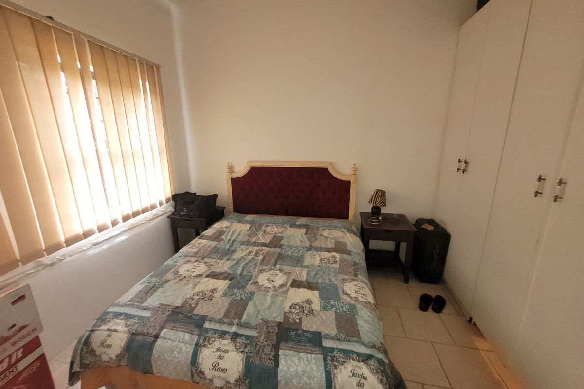 A functional bedroom featuring tiled flooring, a built-in wardrobe for storage, and vertical window blinds providing natural light control.