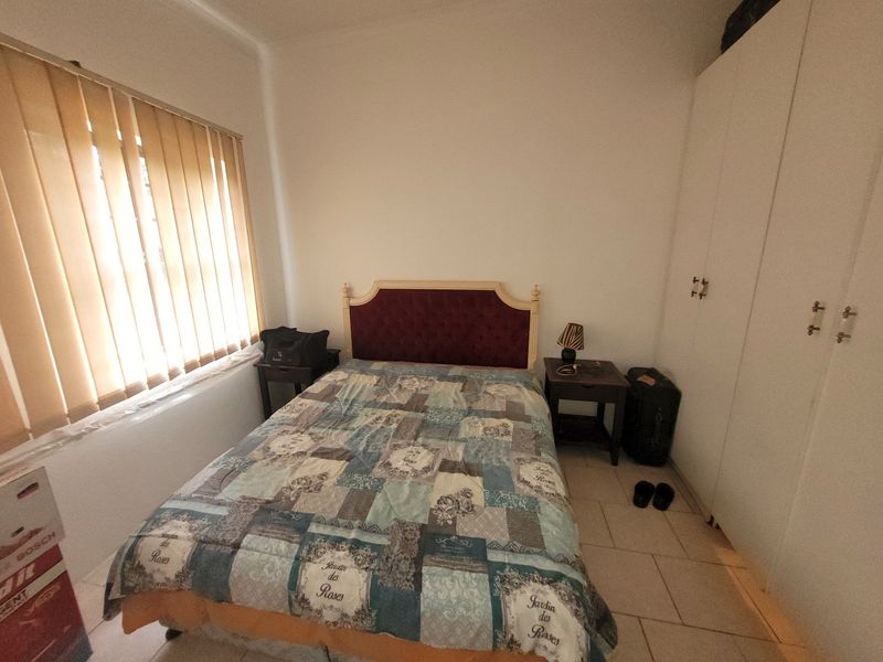 A functional bedroom featuring tiled flooring, a built-in wardrobe for storage, and vertical window blinds providing natural light control.