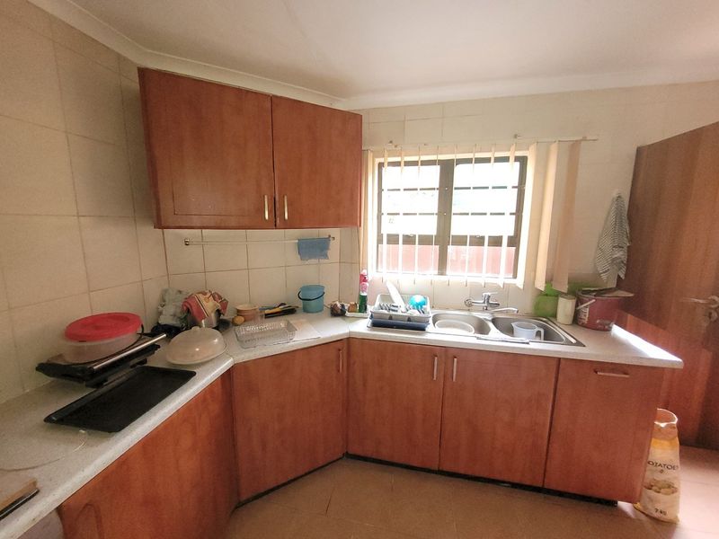 A functional kitchen featuring wooden cabinetry, laminate countertops, and a double bowl stainless steel sink with tiled splashbacks.