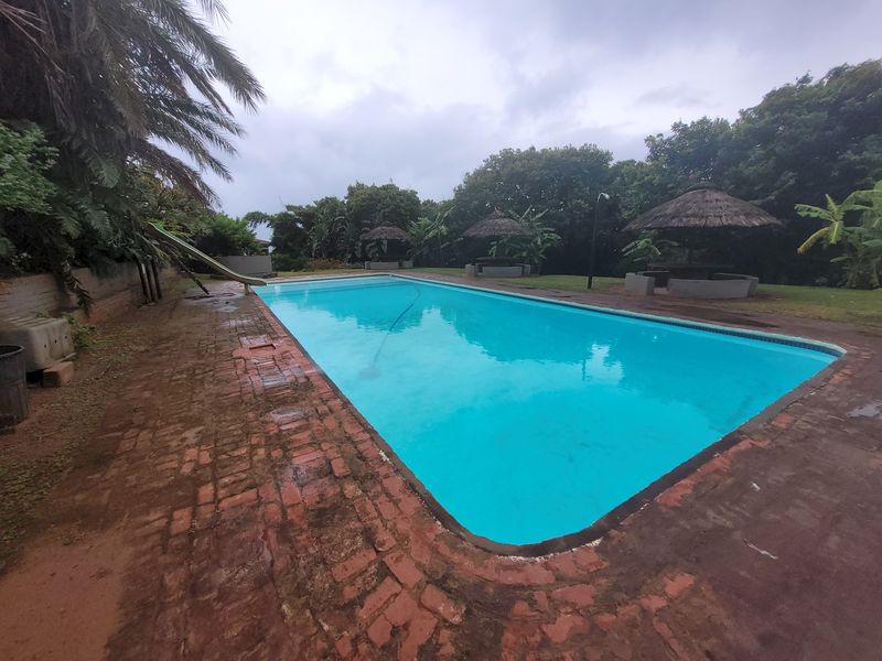Outdoor swimming pool area featuring brick paving, a pool slide, and thatched gazebos set within a landscaped garden environment.