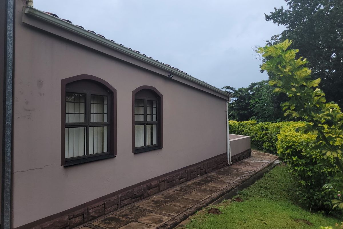 Rear exterior view of the townhouse featuring arched windows, stone cladding base, and a paved walkway alongside a landscaped garden.
