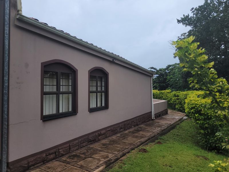 Rear exterior view of the townhouse featuring arched windows, stone cladding base, and a paved walkway alongside a landscaped garden.
