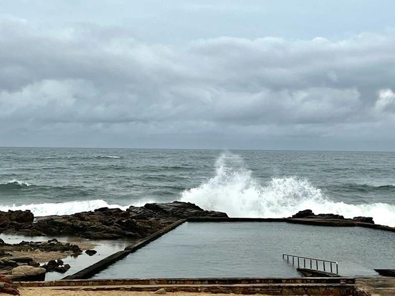 A coastal swimming pool set against the ocean, featuring a built-in metal ladder and natural rock surroundings.