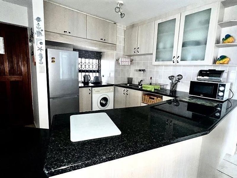 Compact kitchen featuring granite countertops, built-in cabinetry, integrated sink, and space for a washing machine, offering a functional layout for apartment living.