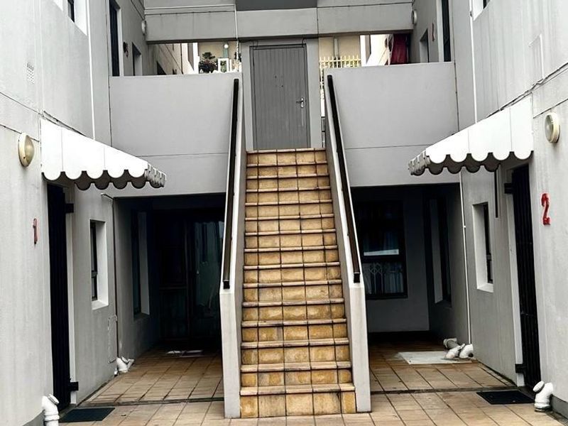 Exterior view of an apartment complex courtyard featuring a central tiled staircase providing access to upper-level units with covered walkways.