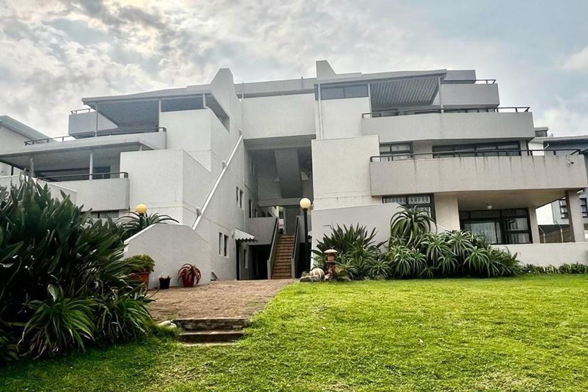 A view of the apartment complex exterior featuring multi-level balconies, concrete facade, and landscaped garden area with paved access path.