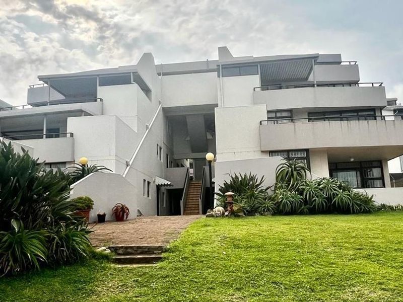 A view of the apartment complex exterior featuring multi-level balconies, concrete facade, and landscaped garden area with paved access path.