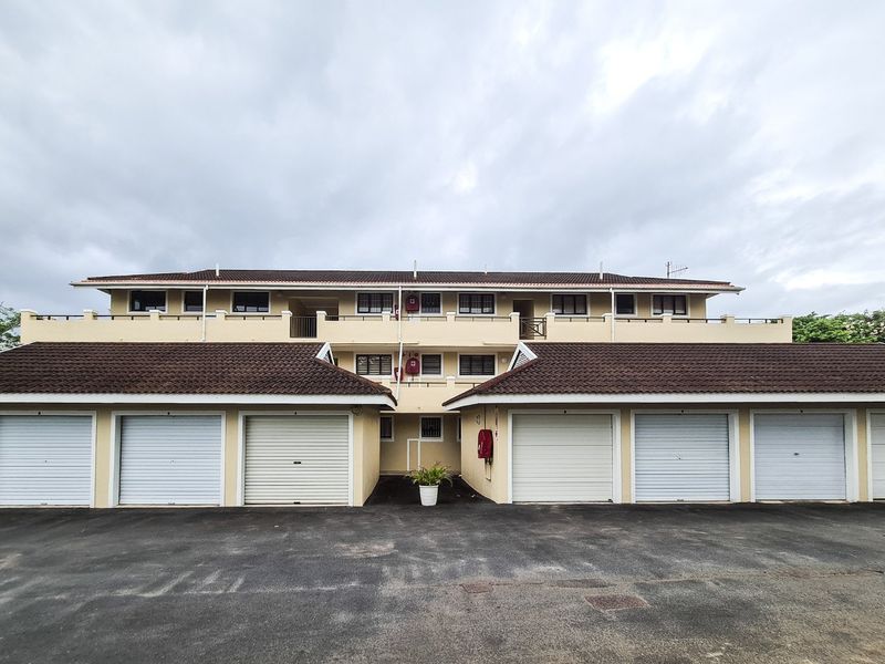 Front elevation of a multi-story apartment complex featuring a row of individual roller shutter garages and upper-level balcony access.