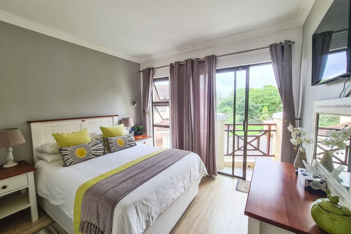A well-maintained bedroom featuring laminate flooring, neutral walls, and direct access to a private balcony through sliding glass doors.