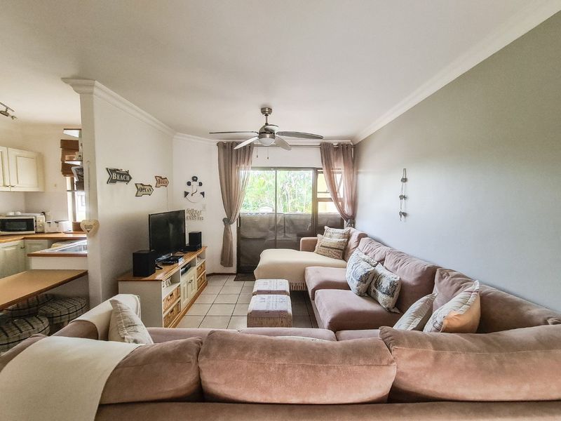 Open-plan living area featuring tiled flooring, a ceiling fan, and direct access to a balcony, with an adjacent kitchen space.