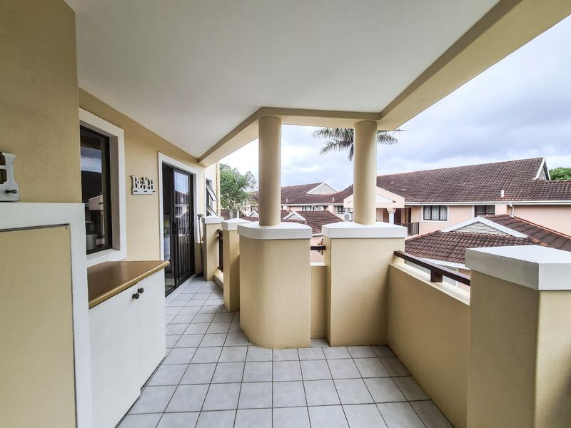 A covered balcony featuring tiled flooring, built-in cabinetry, and concrete columns, offering an outdoor space with views of the surrounding residential complex.