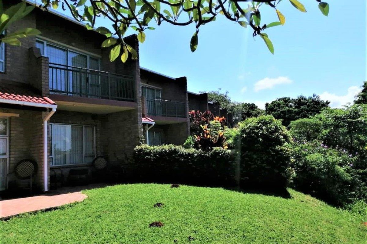 Rear view of the townhouse featuring a brick facade, private balconies with metal railings, a paved patio area, and a well-maintained garden.