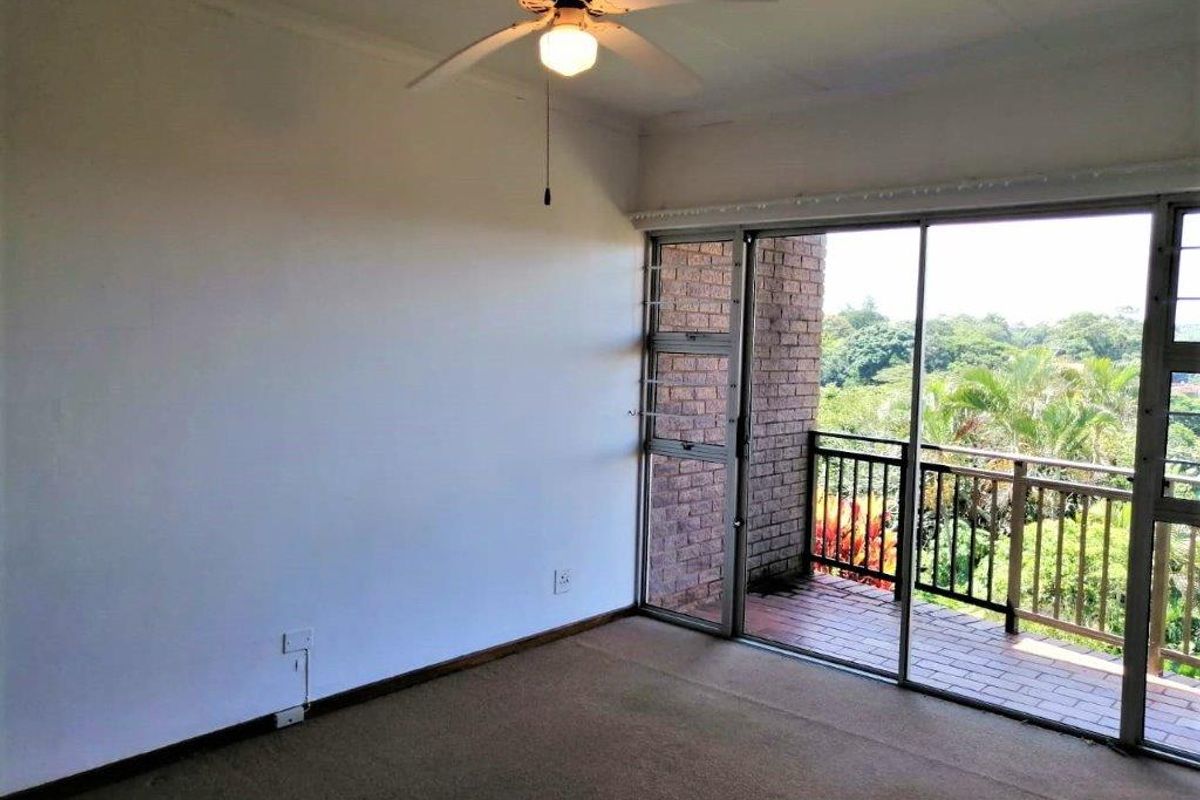 An empty bedroom featuring a ceiling fan, carpeted flooring, and a sliding glass door leading to a private balcony with exterior brick detailing.