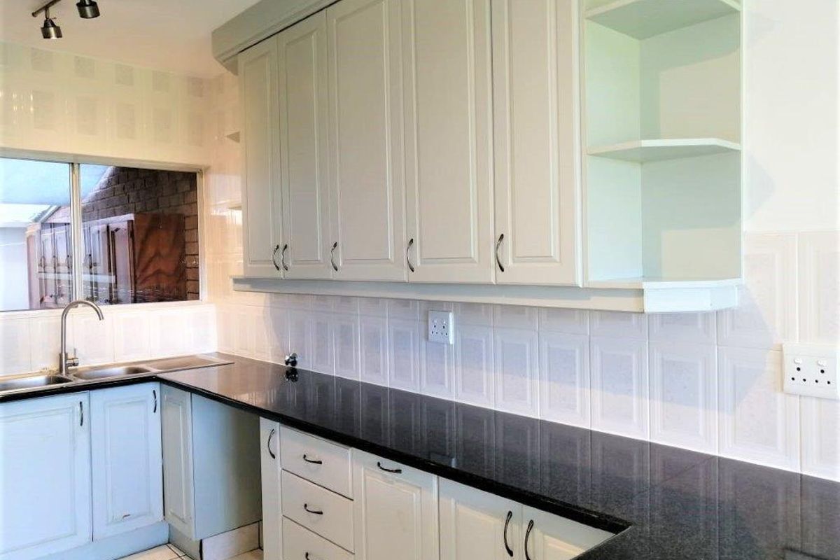 A clean, functional kitchen featuring ample built-in cabinetry, dark granite countertops, a stainless steel sink, and neutral tiled backsplash and flooring.
