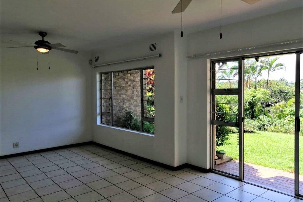 Spacious living area featuring tiled flooring, ceiling fans, and large windows with direct access to the garden through a sliding glass door.