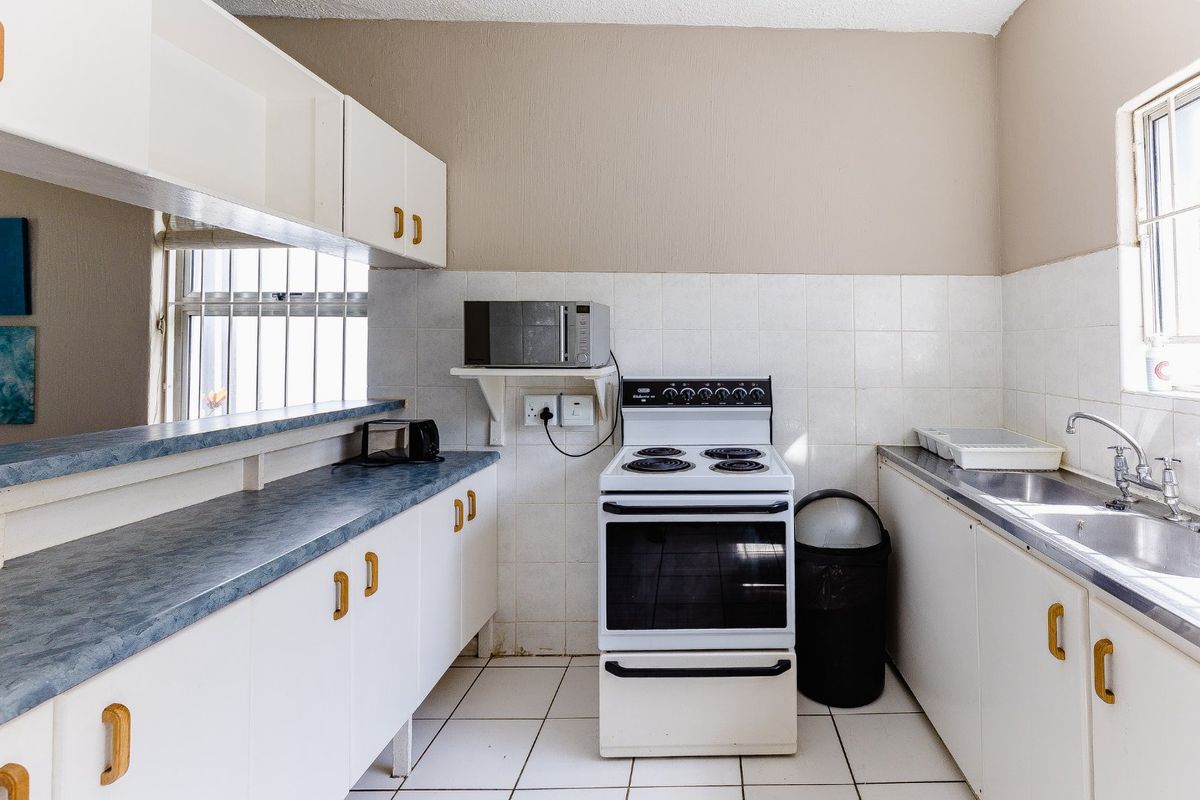 A functional kitchen featuring white cabinetry, a freestanding stove, tiled splashbacks, and a double-basin stainless steel sink with a window view.