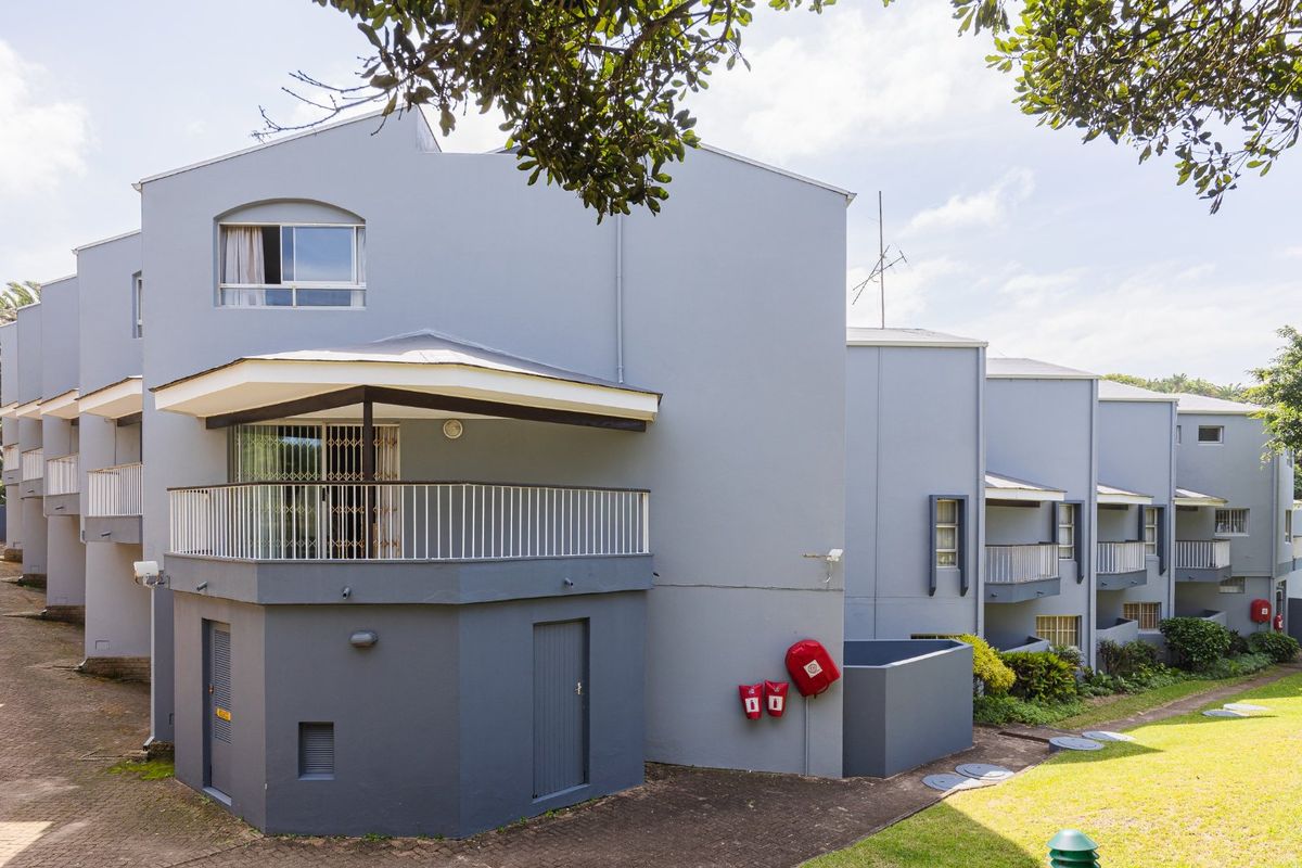 Exterior view of a multi-level apartment complex featuring balconies, paved walkways, and well-maintained communal garden areas.