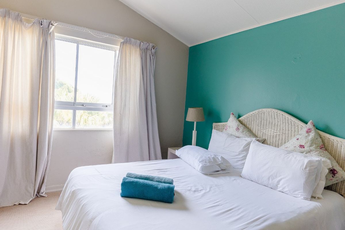 A bright bedroom featuring a teal accent wall, neutral carpeting, and a large window allowing for natural light.