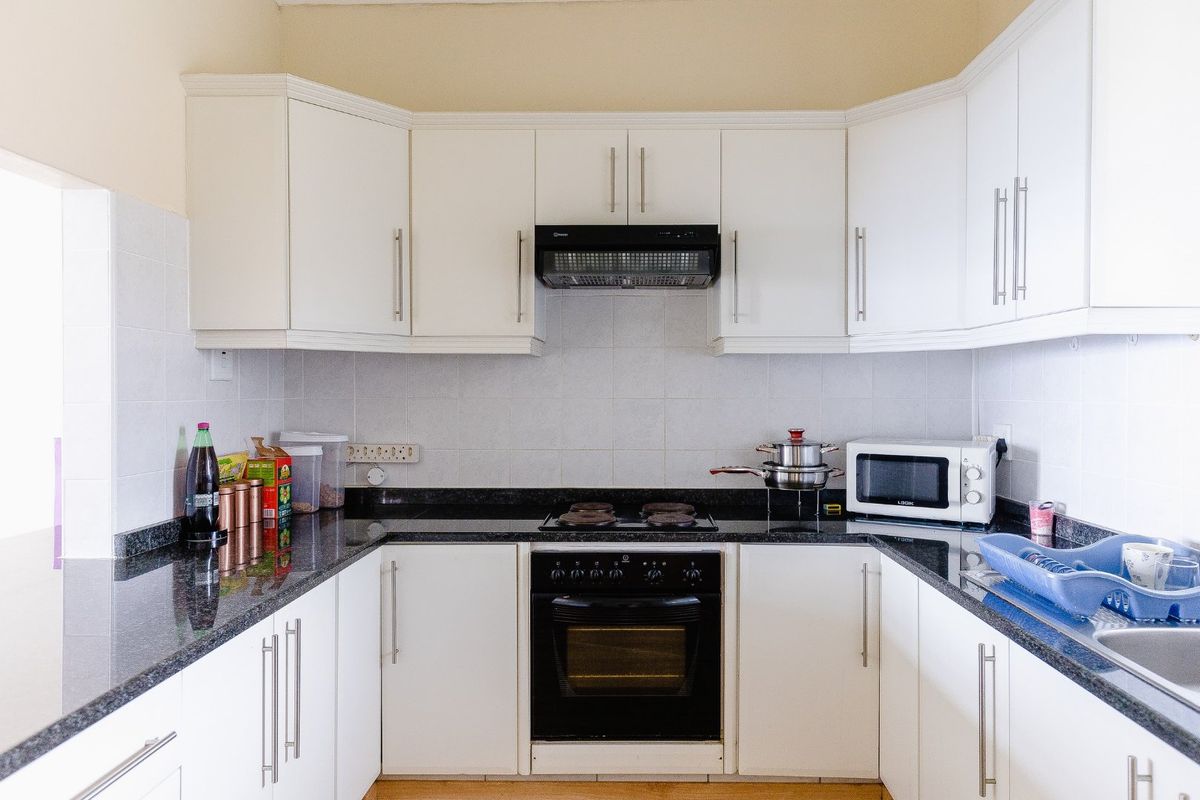 A functional U-shaped kitchen featuring white cabinetry, dark granite countertops, a built-in oven, electric hob, and a tiled backsplash.