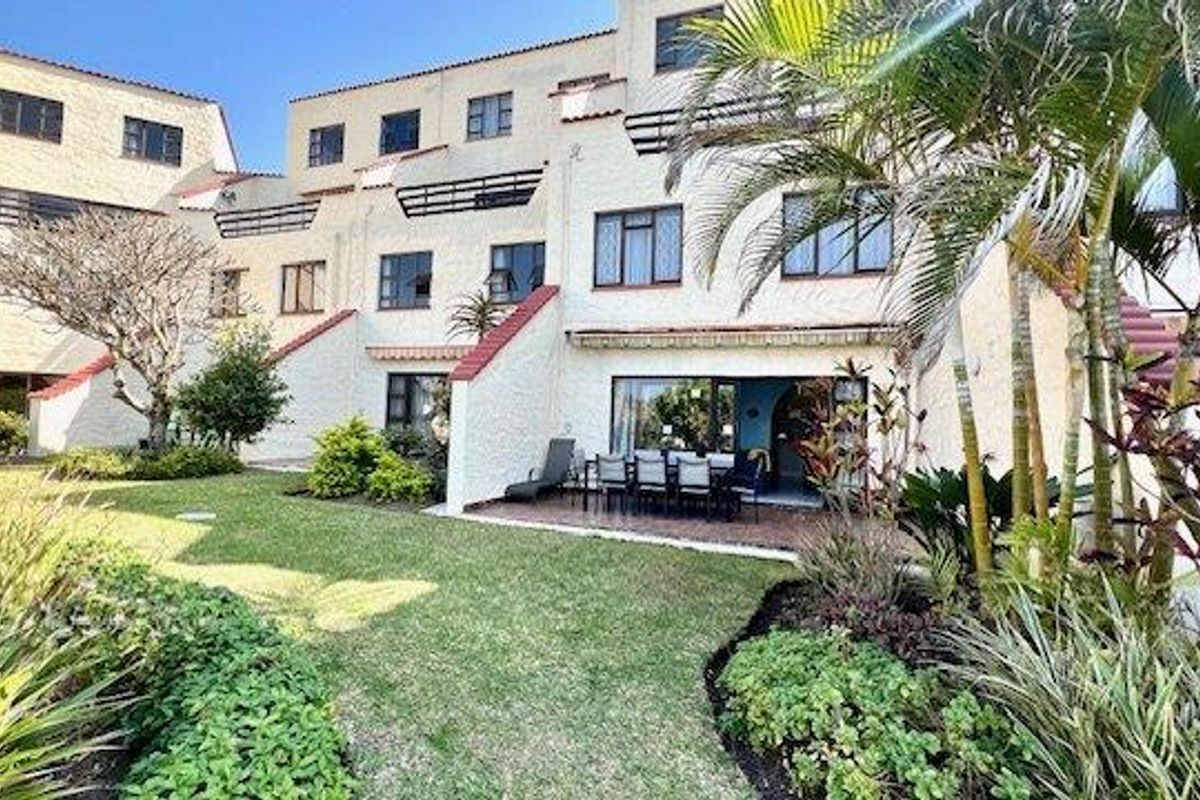 Rear view of the townhouse complex featuring a private tiled patio, landscaped garden, and multi-level balconies with sliding glass door access.