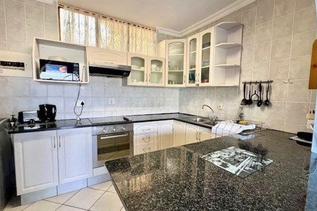 A functional kitchen featuring granite countertops, built-in oven, extractor fan, and ample cabinetry with a tiled backsplash.