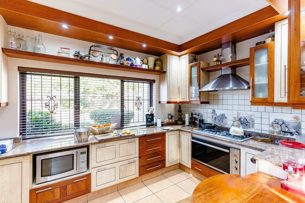 A functional kitchen featuring granite countertops, timber cabinetry, built-in oven, gas hob, and a stainless steel extractor fan with tiled splashback.
