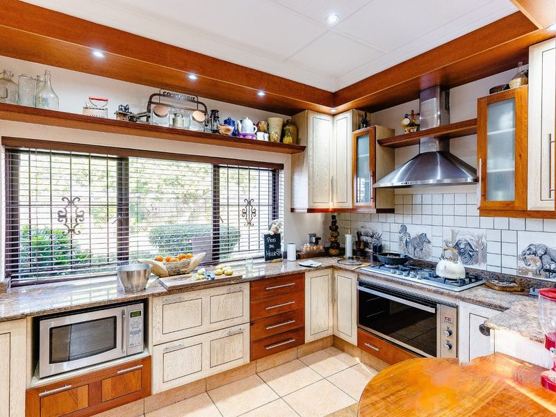 A functional kitchen featuring granite countertops, timber cabinetry, built-in oven, gas hob, and a stainless steel extractor fan with tiled splashback.