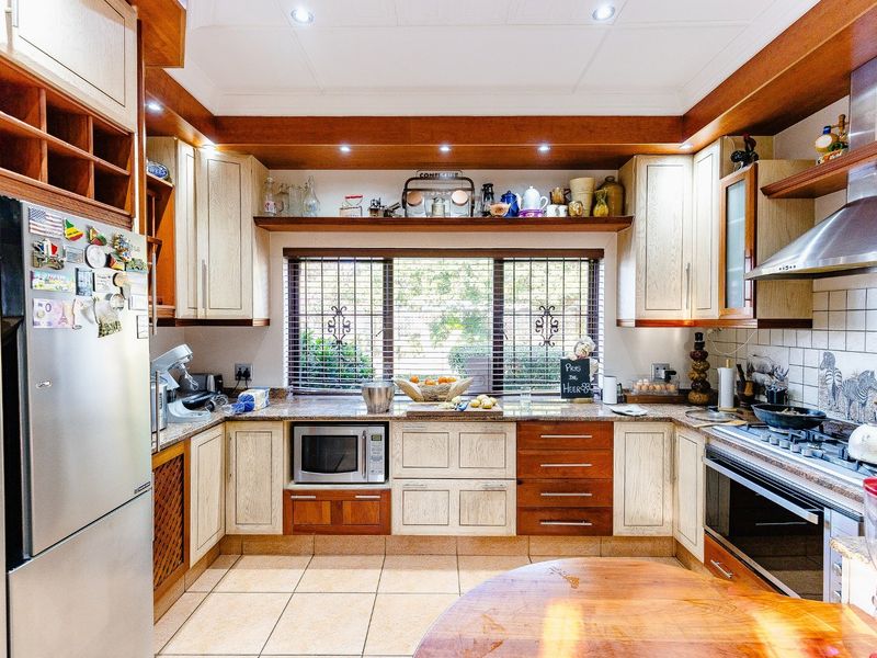 A functional kitchen featuring wooden cabinetry, granite countertops, built-in oven, gas hob, and stainless steel extractor fan, with tiled flooring and natural light.