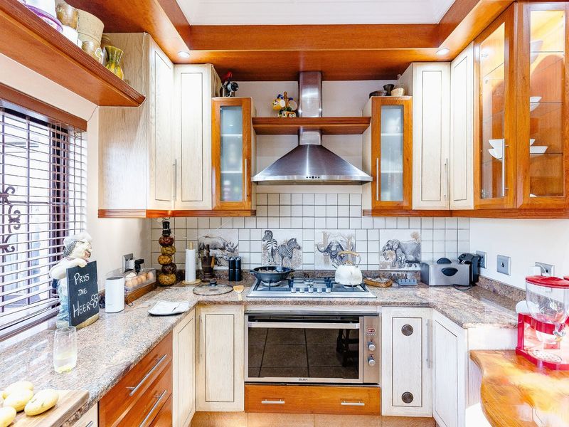 A well-maintained kitchen featuring two-tone cabinetry, granite countertops, a gas hob, and a stainless steel extractor fan with decorative tiled backsplash.