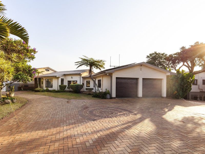 Front view of the property featuring a spacious paved driveway, double garage, and well-maintained brick exterior with mature landscaping.