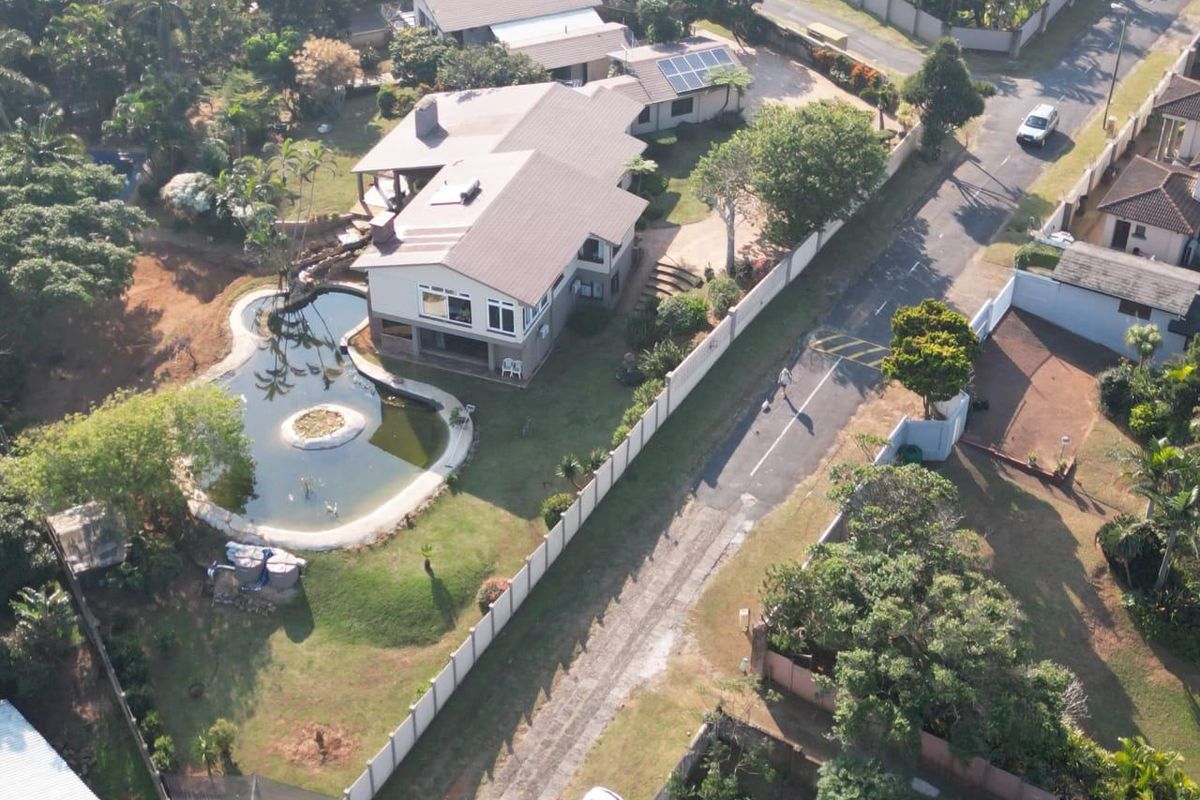 Aerial view of a residential property featuring a large swimming pool, solar panels, tiled roof, and a secure boundary wall.