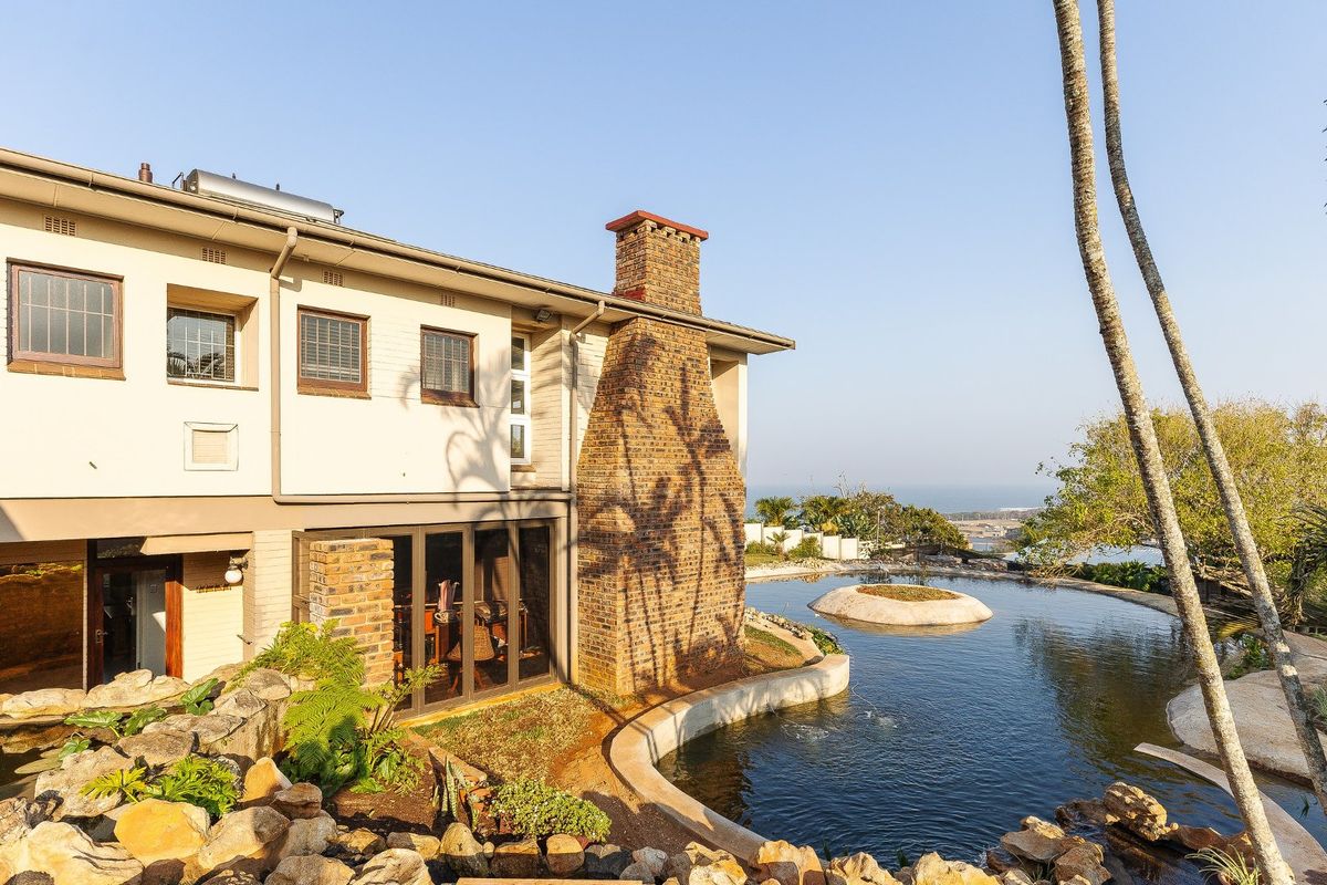 Rear view of the property featuring a large pond, rock garden, brick chimney, and sliding glass doors leading to the interior.