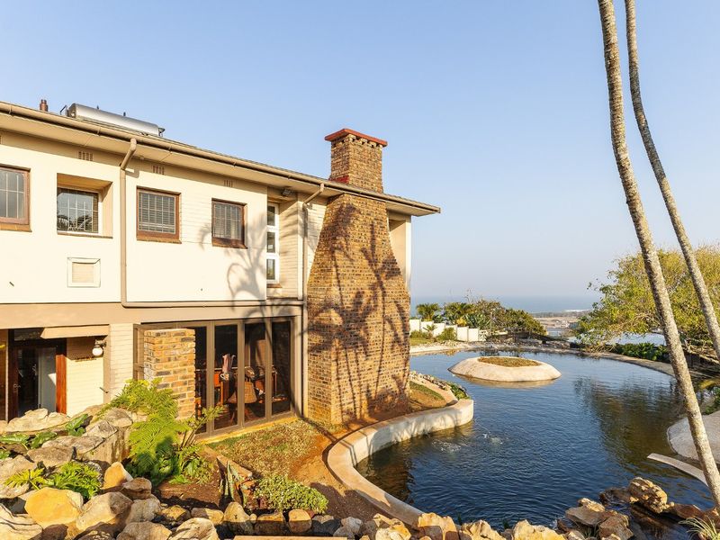 Rear view of the property featuring a large pond, rock garden, brick chimney, and sliding glass doors leading to the interior.