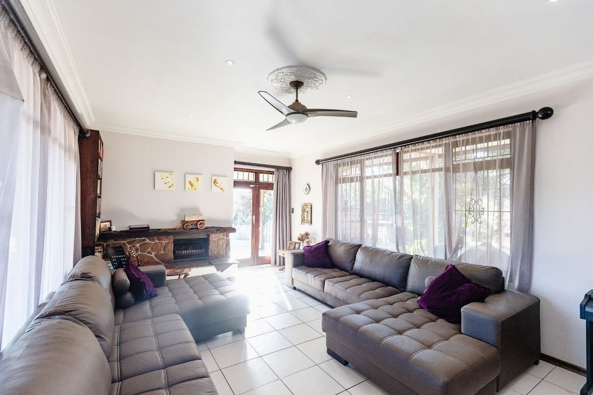 Spacious living room featuring a stone fireplace, tiled flooring, ceiling fan, and large windows providing ample natural light.