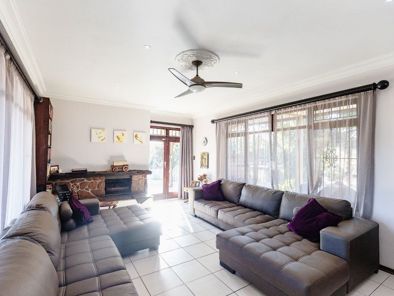 Spacious living room featuring a stone fireplace, tiled flooring, ceiling fan, and large windows providing ample natural light.